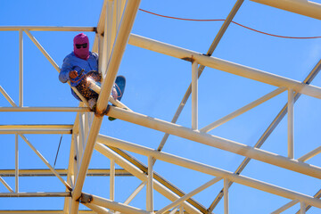 Low angle view of Asian welder welding metal on building roof structure in construction site...
