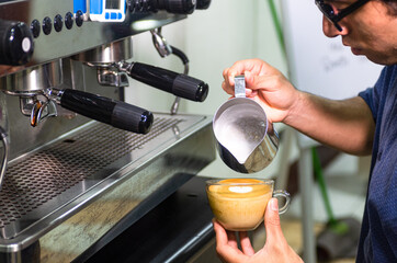 Hand of barista making latte or cappuccino coffee, pouring milk making latte art.