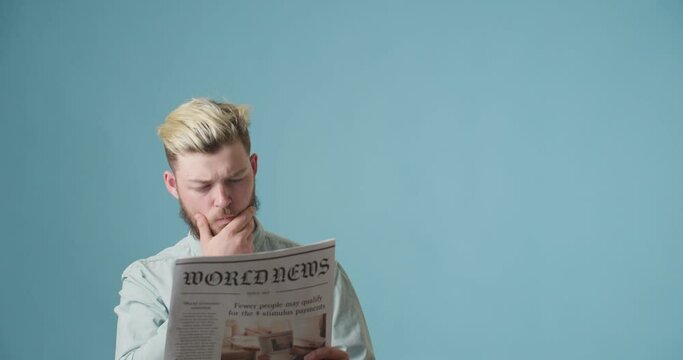 Emotional young man reading newspaper on color background