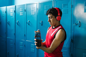 young hispanic disabled man holding a bottle of water in the locker room with hand hypoplasia in...