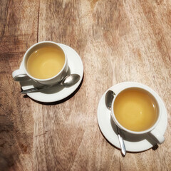 Two cups of tea are on white saucers on a wooden table.