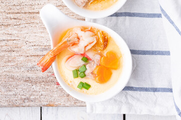 Homemade style steamed egg with shrimp and vegetables in a ceramic bowl on wooden table. healthy food concept.