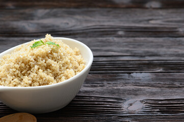 Bowl of boiled quinoa on wood background