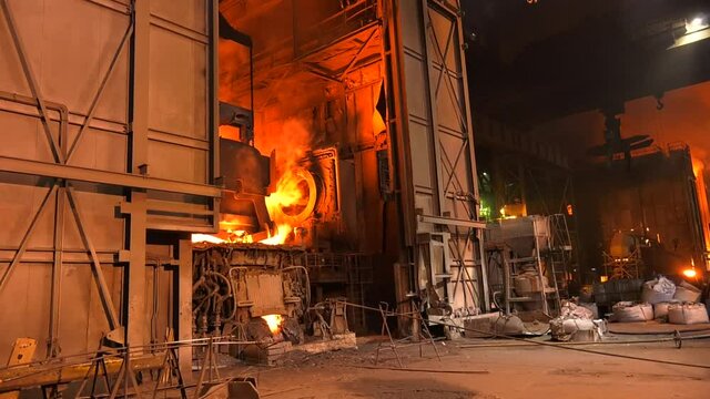 Steel metallurgical factory or foundry workshop interior with big ladle container with molten iron moving on beam crane from blast furnace to mold. Pouring liquid metal in an open-hearth workshop.
