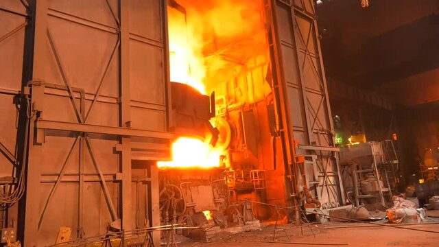 Steel metallurgical factory or foundry workshop interior with big ladle container with molten iron moving on beam crane from blast furnace to mold. Pouring liquid metal in an open-hearth workshop.
