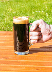 a cup of dark beer on a orange table on a natural green background, pinta of black stout close up, glass of ale