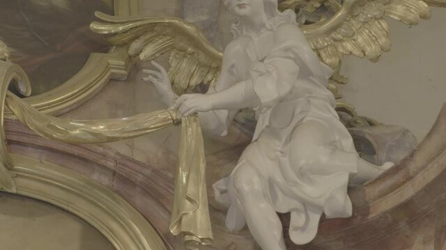 Camera pans to the sculpture of a white angel with golden wings on a baroque altar