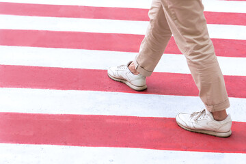Fototapeta na wymiar A woman in sportswear crosses a pedestrian crossing in red and white colors in the city.