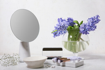 Vase with bouquet of beautiful hyacinth flowers, mirror and cosmetics on table