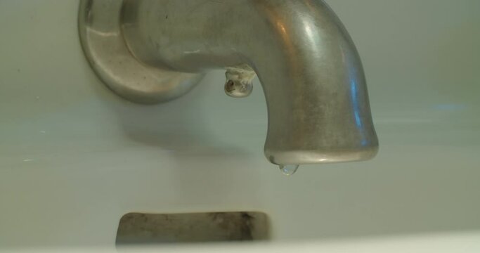 Slow motion medium shot of faucet as a single drop of water falls.