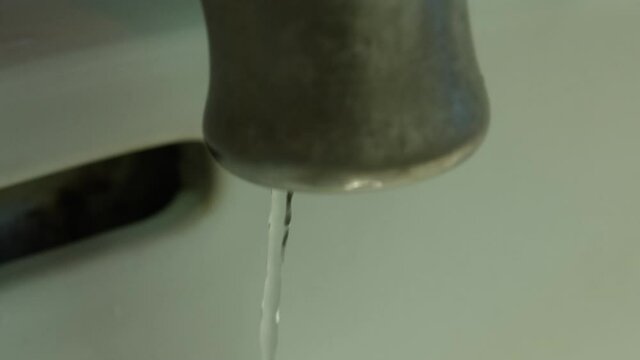 Slow motion medium closeup of a faucet as the water runs and then slowly shuts off.