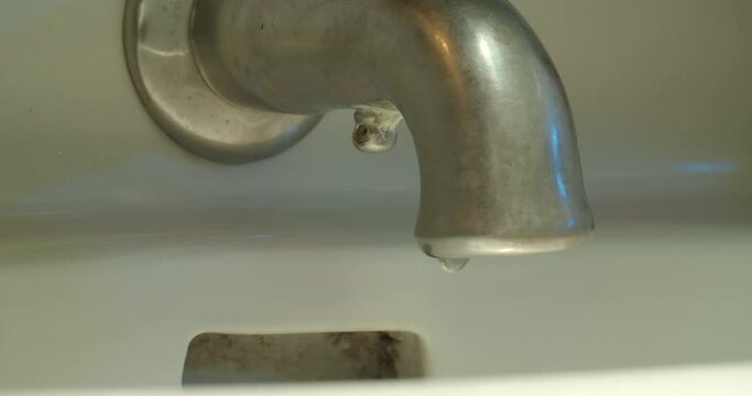 Medium shot of a faucet as the water runs, is turned off and drips.