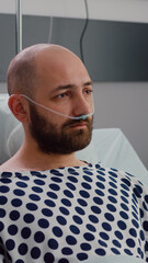 Sad sick man with nasal oxygen tube resting in bad looking into camera during respiratory...