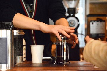 Fototapeta na wymiar コーヒーショップのカウンターでフレンチプレスを使ってコーヒーを入れる、美しい指の男性バリスタ