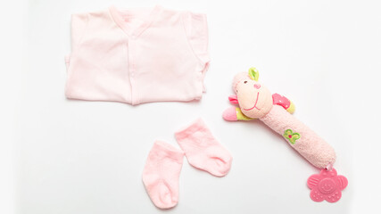 Child birth. Pink clothes for little girl - bodusuit and socks. Accessories for newborn. Baby thing and toy on white background. Flat lay. Top view.