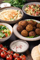 Middle eastern or arabic cuisines, falafel, hummus, tabouleh, pita and vegetables on wooden background, selective focus