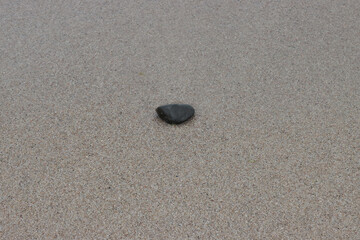 Fototapeta na wymiar Black stone on wet beach sand.