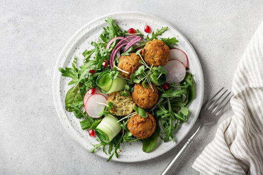 Falafel and fresh vegetables salad on a white ceramic plate on concrete background, view from above. 