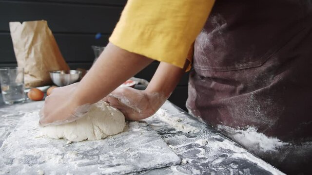 Close up shot of unrecognizable Afro-American female baker kneading dough, sifting flour and then clapping her hands while preparing bread in kitchen