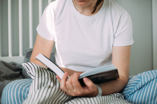Young woman reading book on bed at home. Concept of cozy, comfort home. Lifestyle, slow living