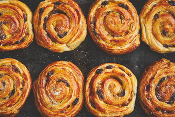Homemade puff pastry cinnamon rolls with raisins placed on oven iron tray