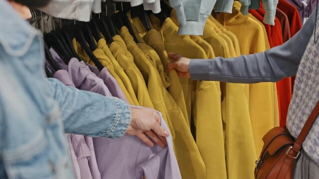 Close-up of unrecognizable couple sorting hoodies of vibrant colors hanging on rail in clothing shop looking for right size