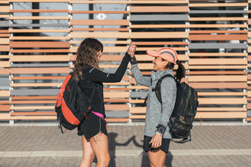 Two happy friends greeting and meeting on the street. Meeting to go for a run, carrying a backpack with sportswear.