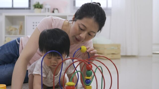 Close Up Asian Baby Girl Is Staring With Concentration And Grabbing The Bead Roller Coaster As Her Mother Is Teaching Her How To Play With It Behind Her.