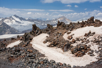 Pieces of solidified lava of the Elbrus volcano against the background of mountains and glaciers of the Main Caucasian ridge. Large chunks of solidified lava are reminiscent of a volcanic eruption in