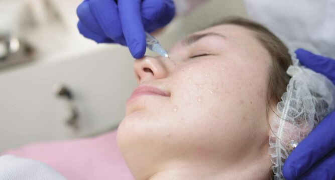 Hands of beautician doctor dripping anti-aging oil serum from syringe on woman face. Facial anti wrinkle skin care. Close up of young woman at cosmetology clinic, having beauty procedures.