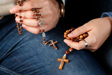 Catholic man and woman praying together at home. Close up on hands with prayer beads.   France.