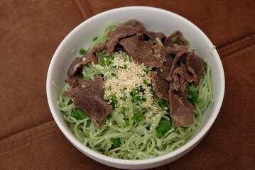 Spinach noodles with slices of meat and sesame seeds sprinkles.