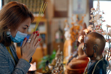 Tu An buddhist temple.  Woman wearing surgical mask praying with encens sticks.  France.