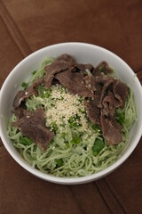 Spinach noodles with slices of meat and sesame seeds sprinkles.