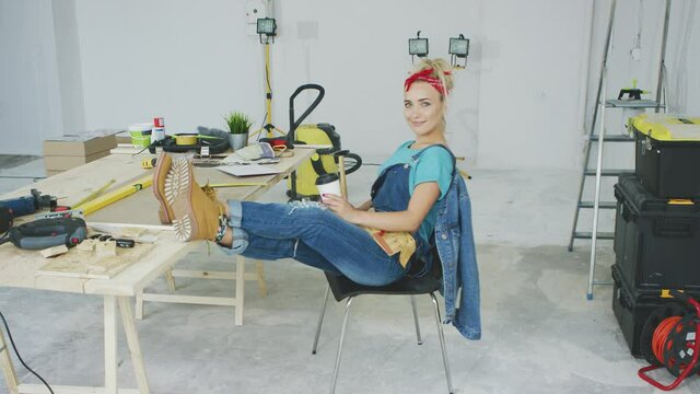 Woman resting with smartphone at carpenter workbench