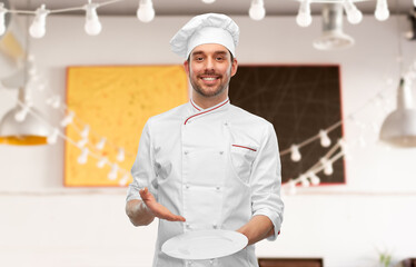 cooking, culinary and people concept - happy smiling male chef in toque holding empty plate over restaurant background