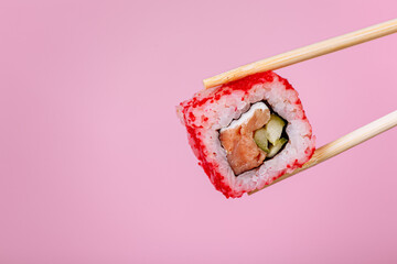Tasty sushi roll California with wooden chopsticks on pink background close up. Place for caption and text