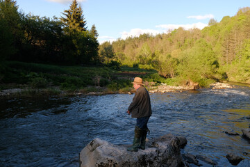Senior man with a hat fishing in the mountain river on a fishing lure
