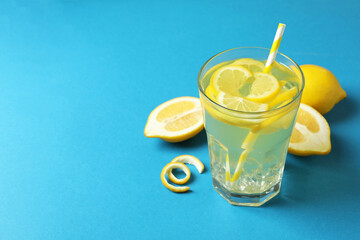 Glass of lemonade, straws and lemons on blue background
