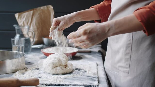 Close up shot of hands of unrecognizable woman kneading dough on table in bakery kitchen