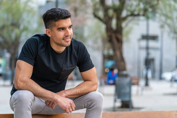 Hispanic young man sitting on a bench in the city