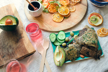 Layout of snack plate and boards with linen breads, fresh vegetables, dried fruits, fruit candies, two glasses of pink vitamin water and two wooden forks.