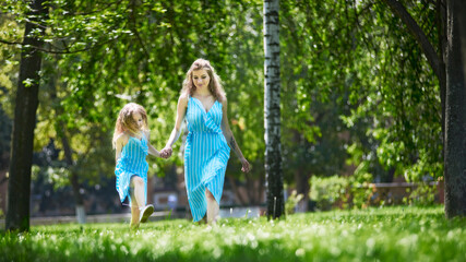 Fototapeta premium Happy mother and daughter walking in the park holding hands