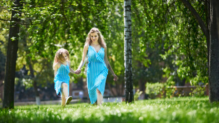 Happy mother and daughter walking in the park holding hands