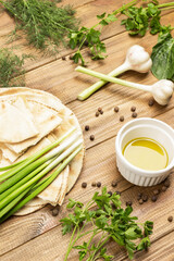 Green onions on pita bread. Olive oil in white bowl. Garlic, greens and sweet peas on table.
