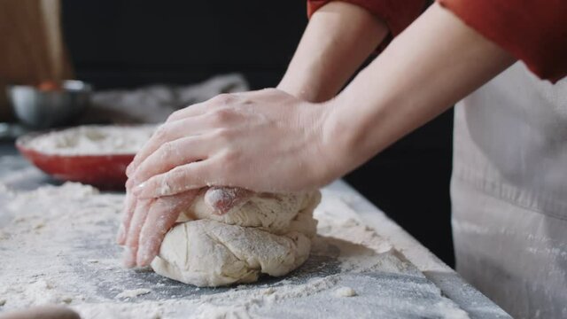 Close up view of hands of female bakery chef adding flour while kneading dough on kitchen table