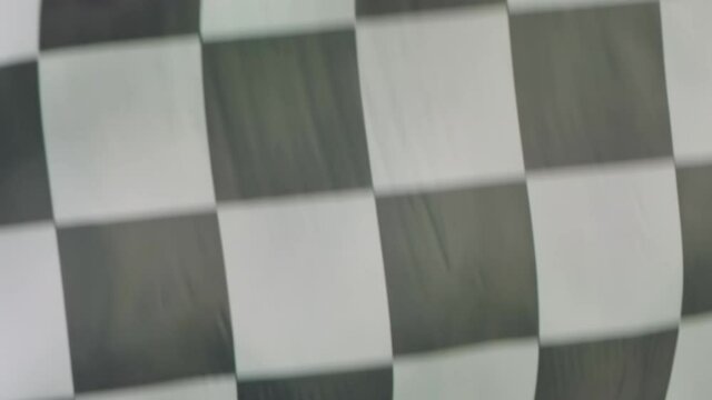 Silk black and white checkered flag of the start or end of car racing flies against a green screen background. Blurred racing flag flutters in the wind. Slow motion. Close up.