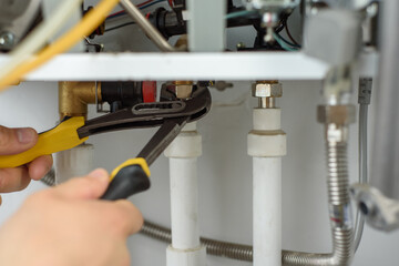A man with tools checks the pipes that fit the gas heating boiler.