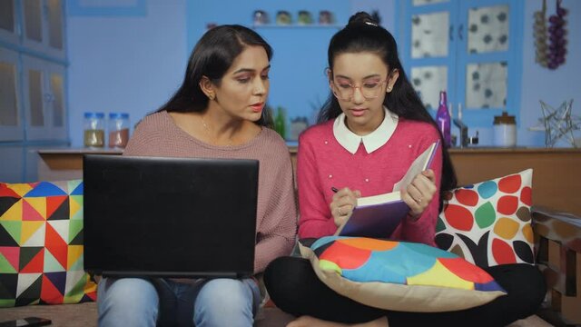 Working lady helping her daughter in studies while doing her office work from home. Medium shot of a teenage girl sitting on the sofa studying while her mother working on laptop - remote work and l...