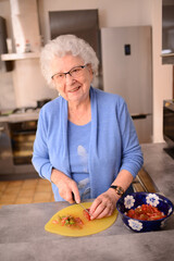 smiling and happy senior woman at home in her kitchen cooking chopping and slicing organic vegetable with a knife